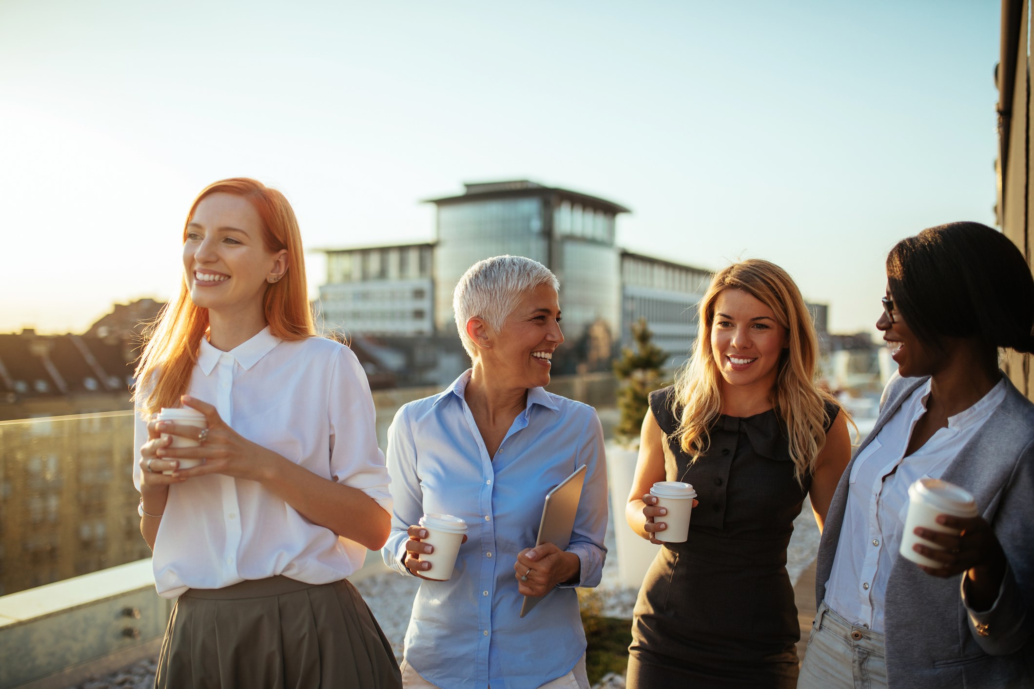 four female collegues drinking coffee and chatting laughing